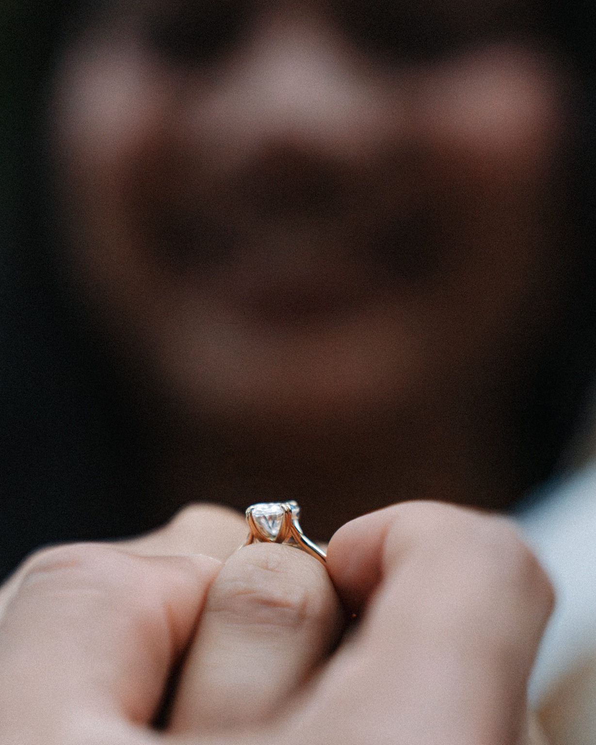 Close-up of Maggi’s engagement ring with her smiling face softly out of focus behind it