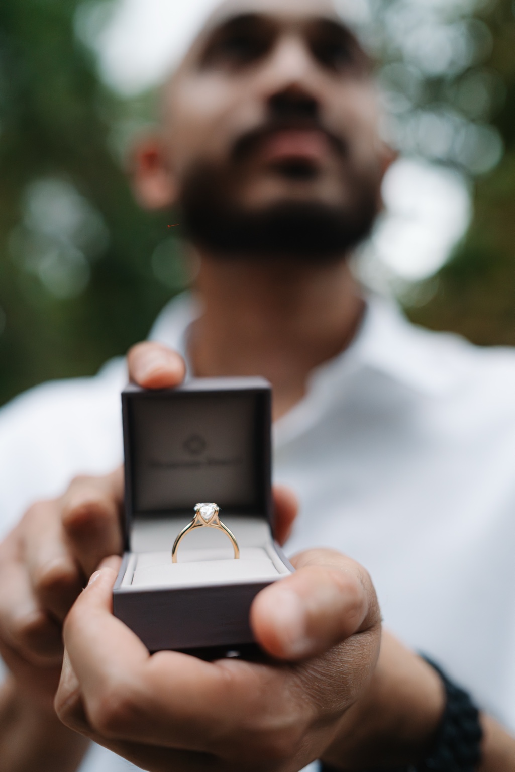 Akhil holding an open box with a gold engagement ring toward the camera