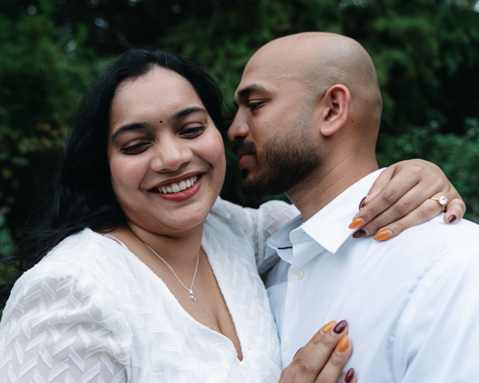Maggi smiling with her arm around Akhil and her engagement ring visible against his white shirt