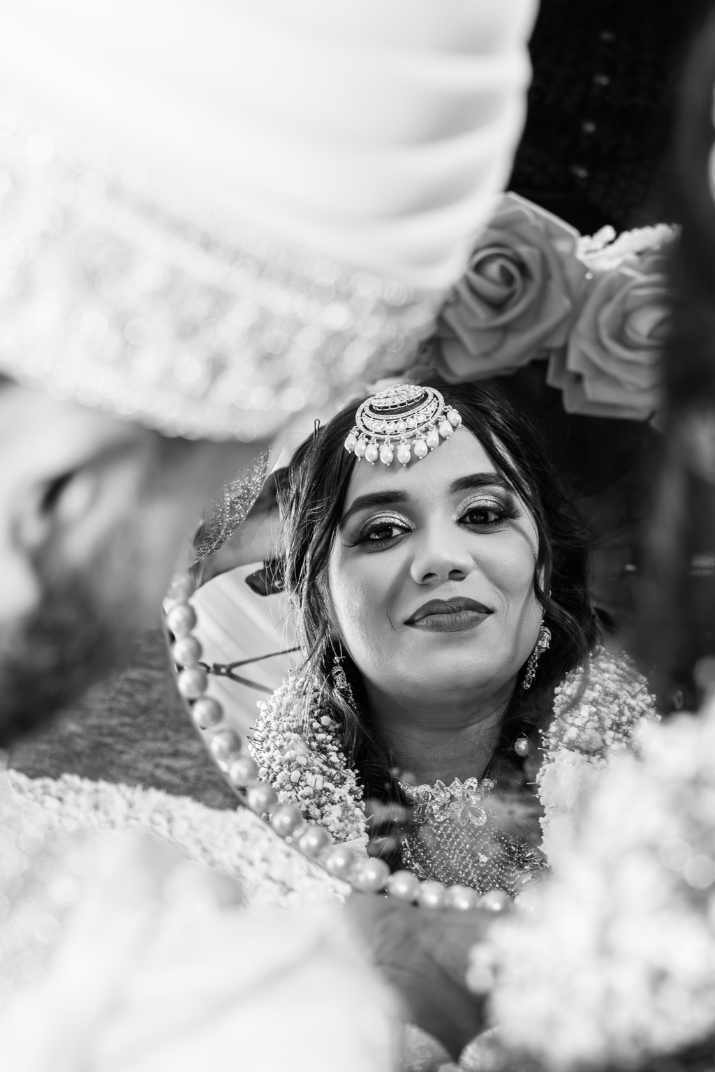 Black-and-white portrait of a bride wearing ornate jewelry beneath a draped veil