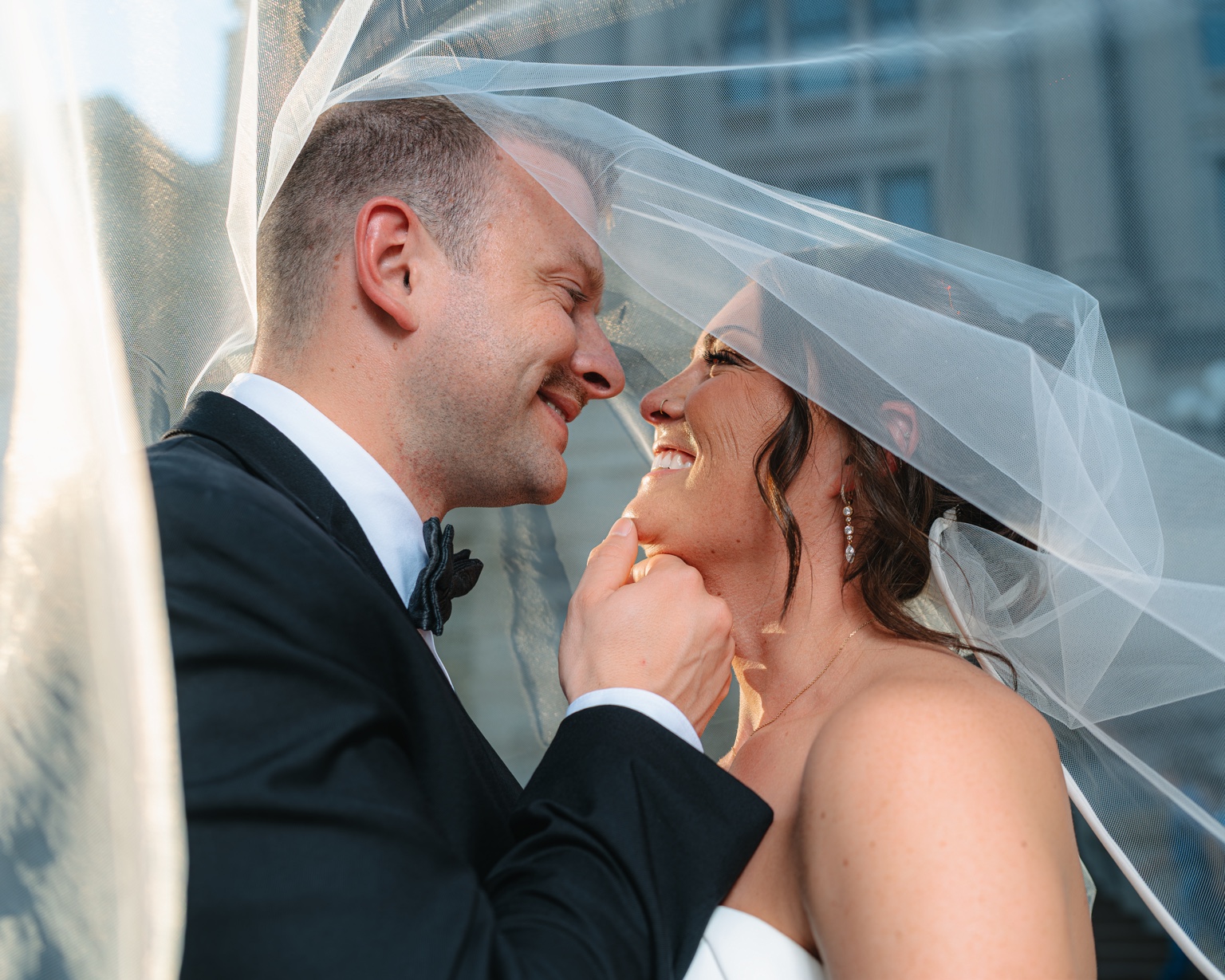 A couple kiss beneath a soft wedding veil