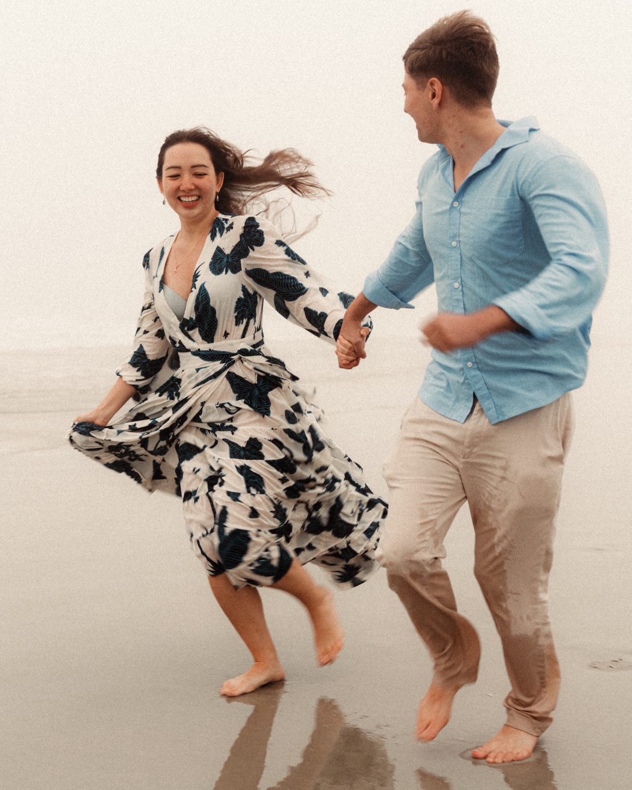 Engaged couple running hand in hand across wet sand at New Smyrna Beach, Florida