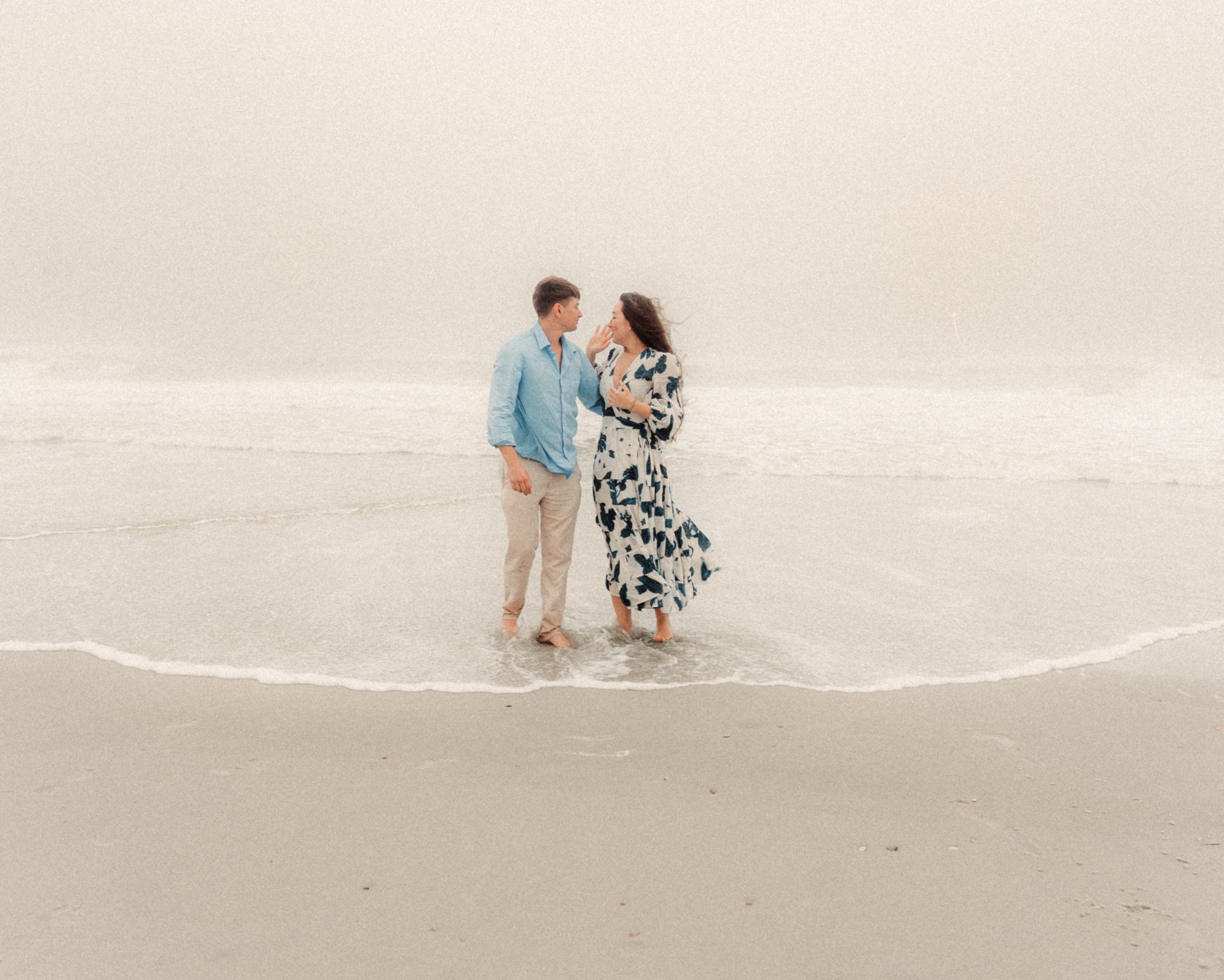 Engaged couple standing together in gentle surf on a misty shoreline at New Smyrna Beach, Florida
