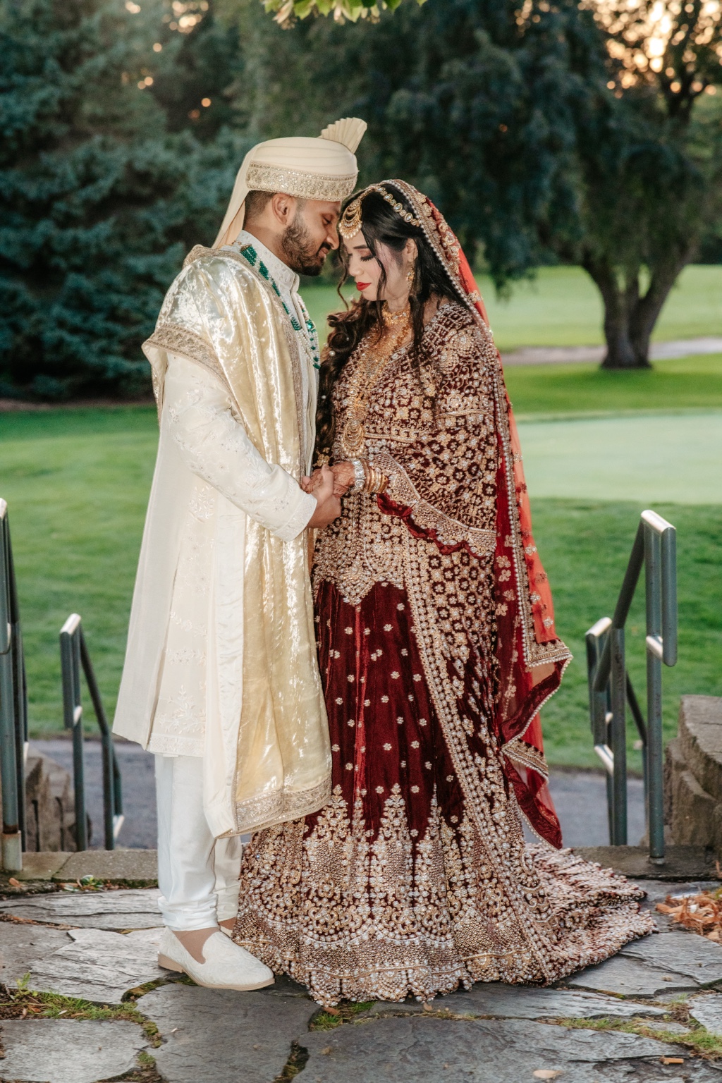 A wedding couple in ornate traditional attire standing together in a garden