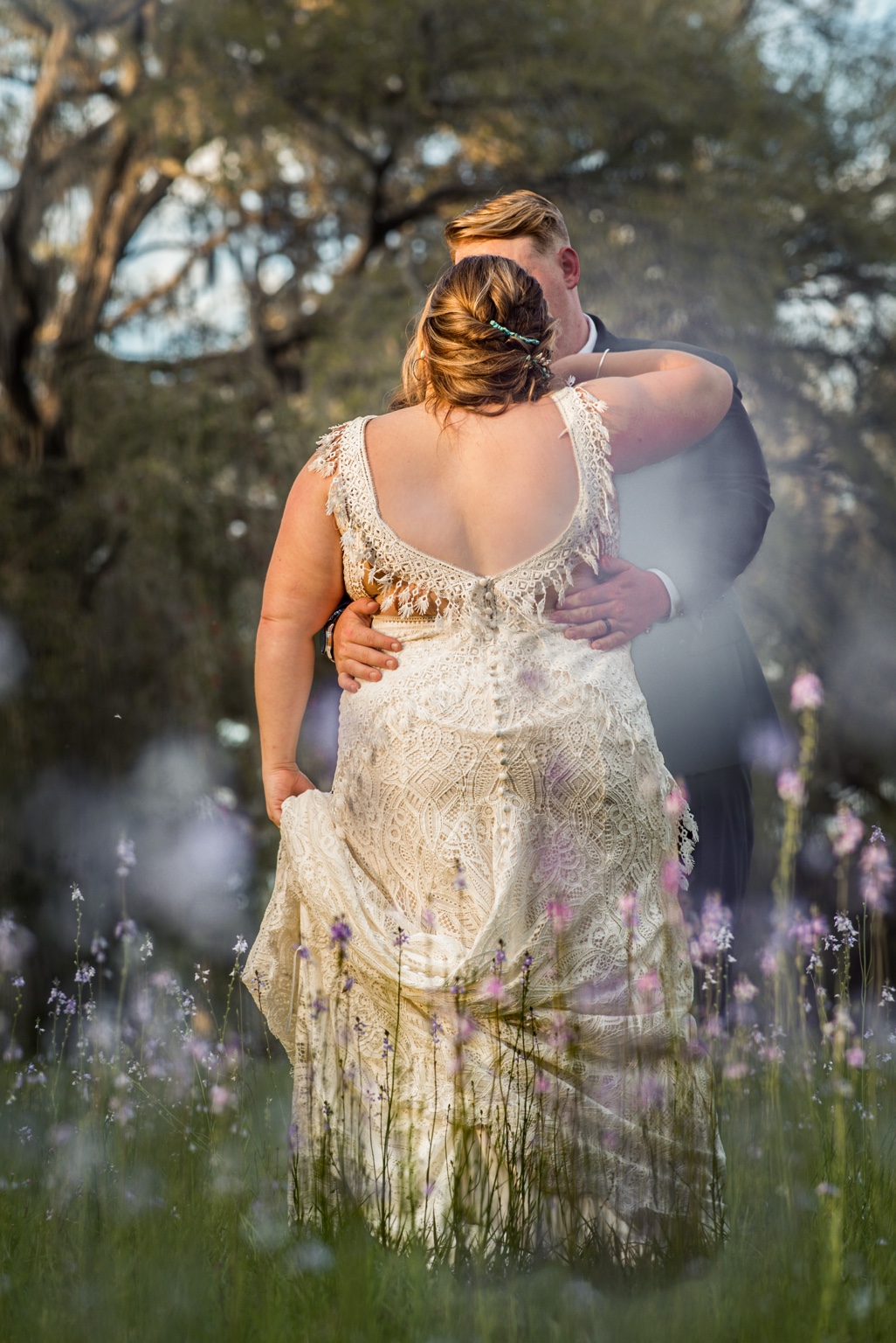 Newlyweds embracing in a layered wedding portrait with trees and purple wildflowers